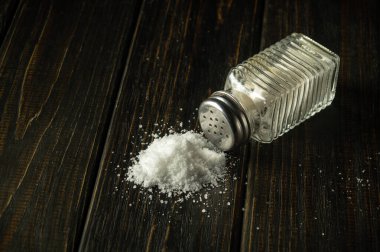 Siyah bir masanın üzerindeki tuzluktan bir yığın tuz. Aşırı tuz alımı kavramı diyabetin veya diğer hastalıkların nedeni olabilir..