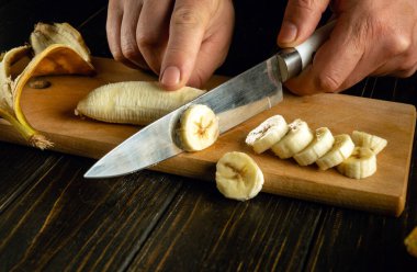 Mutfak tahtasında muz dilimlemek. Bir şefin elinde meyve diyeti yemeği hazırlamak için bir bıçakla..