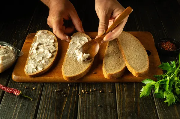 stock image A wooden spoon in the hands of a man for spreading grated lard on rye bread before preparing hearty sandwiches for a snack. Peasant food.