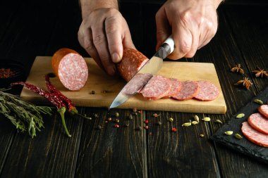 Aşçı elleri bıçakla mutfak masasında salam kesiyor. Restoranda sofra hazırlamak için..