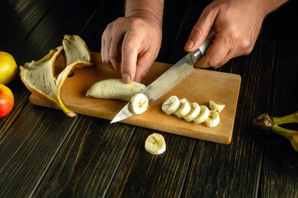 Mutfak masasında meyve tabağı hazırlamak için elinde bıçakla muz dilimlemek. Reklam alanı.