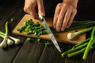 Kesme tahtasındaki bir şefin elinde bıçakla taze sarımsak dilimlemek. Basit bir sebze salatası hazırlama konsepti. Reklam alanı.