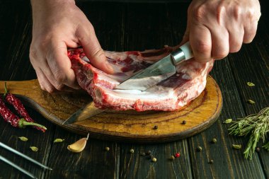 Bıçaklı kasap elleri kesme tahtasındaki kaburgaları kesiyor. Mutfak masasında et pişirme kavramı.