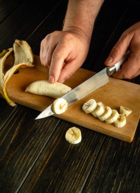 Şefin elleri, akşam yemeği için bir meyve tabağı hazırlamak için olgun bir muzu bıçakla kesti. Siyah bir masa üzerinde reklam için yer.