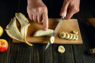 Mutfak tahtasındaki bıçağı kullanan bir şefin elleri diyet menüsü için olgun bir muzu kesti..
