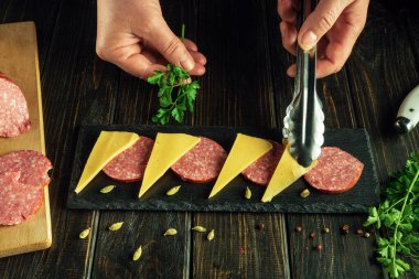 Mutfak masasında maydanozlu sosis ve peynir servis eden siyah tahta..