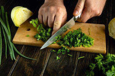 Şef mutfak masasında salata hazırlar ve bıçakla maydanoz doğrar..