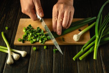 Şefin elleri, vejetaryen yemeği veya salata hazırlamak için kesme tahtasındaki yeşil sarımsağı kesmek için bıçak kullanıyor. Reklam için yer.