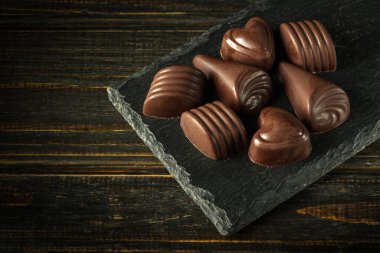 Servis tahtasındaki tatlı siyah çikolata şekerlemeleri. Siyah bir kırsal masa üzerinde reklam için alan.