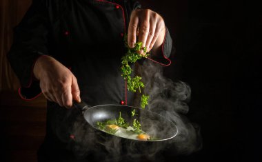 Profesyonel bir aşçı elleriyle çırpılmış yumurtanın içine taze aromalı maydanoz atar. Restoran mutfağında lezzetli bir yemek hazırlama fikri. Reklam için alan.