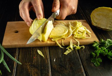 Mutfak masasında taze lahana pişiriyorum. Bir aşçının elinde lahana dilimlemek için bıçak..