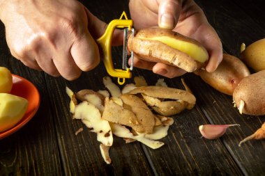 Adamın elleri evdeki mutfakta patates soyacağı ile çiğ patates soyuyor. Patates püresi yapma süreci.