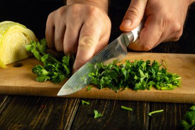 Mutfak masasında lahana olan vejetaryen yemeği için bir şefin elinde bıçakla yeşil maydanoz kesmek..