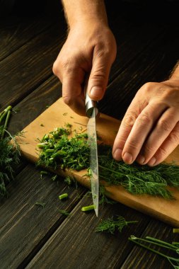 Bir şefin elleriyle vejetaryen yemeği hazırlamak için kesme tahtasındaki yeşil dereotu bıçakla dilimlemek. Reklam alanı.