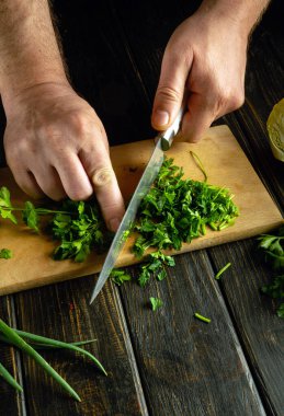 Bir aşçı lezzetli bir kahvaltı hazırlamak için taze maydanozu kesme tahtasının üzerinde bıçakla doğrar..