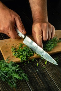 Erkek eli, vejetaryen yemeği hazırlamak için kesme tahtasındaki yeşil dereotu ya da rezene kesmek için bıçak kullanıyor. Köylü yemeği. Boşluğu kopyala.
