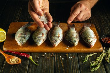 Mutfak masasında balık pişiriyorum. Aşçı elleri kızarmadan önce balığa tuz ekler..