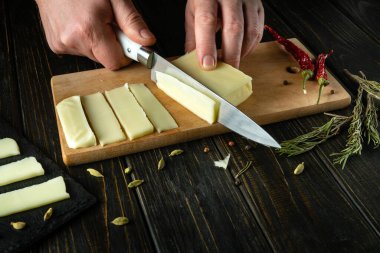 Aşçının eli bıçakla Mozzarella peynirini kesme tahtasında tadımlık olarak küçük parçalara ayırdı. Lezzetli sütlü peynir tarifi sunumu. Boşluğu kopyala.