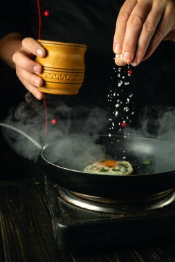 Şef sıcak bir tavaya elle tuz ekliyor. Lokanta mutfağında yumurtayla kahvaltı hazırlama konsepti.