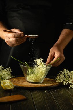 Kvass yapmadan önce bir kase mürver böğürtlenine şeker ekliyorum. Mutfak masasının üstündeki şifalı otlarla dolu bir şifalı bitki uzmanının elinde bir kaşık. Reklam için alan.