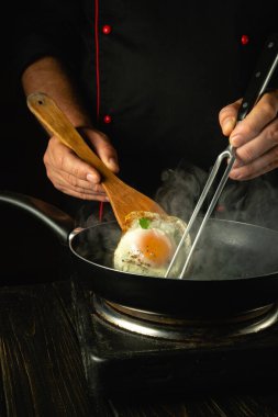 Şef mutfakta çırpılmış yumurta hazırlıyor. Aşçı el, mutfak spatulası kullanarak yumurtayı kızgın bir tavaya çevirir. Basit bir kahvaltı hazırlama konsepti..
