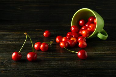 Siyah bir masanın üzerindeki yeşil bardaktan dökülen olgun kirazlar. Gean 'la lezzetli ve sağlıklı tatlı kavramı.