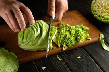 Bir şef, vejetaryen salatası hazırlamak için kesme tahtasındaki taze lahana kesmek için bıçak kullanır..