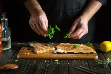 Mutfak masasında balık bifteği, aromalı maydanoz ve şefin ellerinde baharat pişirmek..