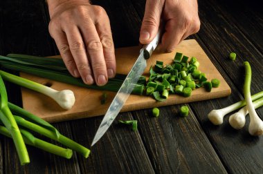 Bir şef, vejetaryen yemeği ya da salata hazırlamak için kesme tahtasındaki genç sarımsağı kesmek için bıçak kullanır..