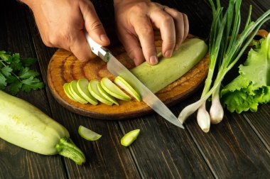 Mutfak masasında vejetaryen yemeği hazırlamak için bir şefin elinde bıçakla kabak dilimlemek. Siyah masadaki reklam alanı.