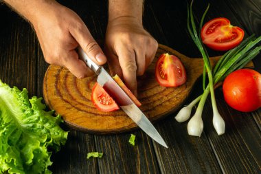 Şef kırmızı domatesi bıçakla kesiyor. Restoranın mutfağında sebze salatası pişirmek. Sebze diyeti fikri.