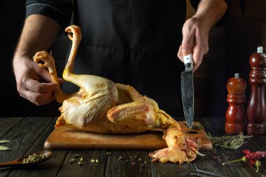 Mutfak masasında çiğ horoz pişirmek. Fırında pişirmeden önce mutfak masasında tavuk kesen bir aşçının elinde bıçak..