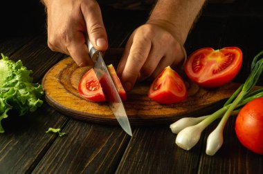 Evde sebze salatası yapmak için domatesleri insan eliyle kesmek. Tahtalardaki reklam alanı.