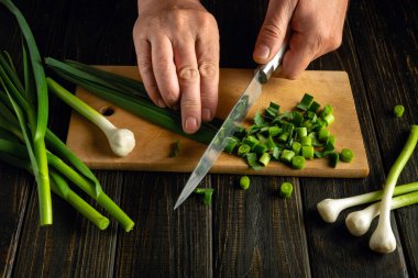 Genç yeşil sarımsağı keserek yiyeceğe ekliyorum. Yemek hazırlayan bir aşçının elinde bıçak..