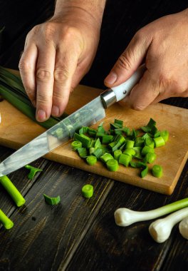Bir şef, vejetaryen yemeği ya da salata hazırlamak için ağaç kesme tahtasındaki yeşil sarımsağı kesmek için bıçak kullanır..
