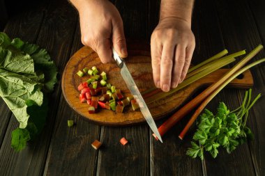 Aşçı mutfak masasında vitamin salatası hazırlıyor. Bir şefin elinin yakın plan fotoğrafı taze ravent saplarını bıçakla kesiyor. Reklam için yer.
