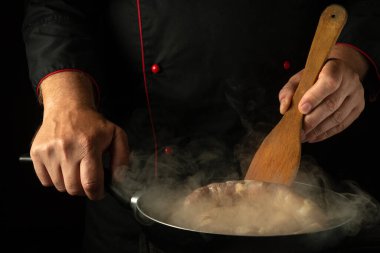 Elindeki ahşap spatulayla şef tavada kızarırken sosisi çeviriyor. Meyhane mutfağında sosis pişirme kavramı.