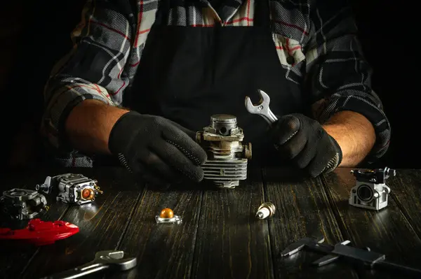 stock image Mechanic in gloves at the table in the workshop repairing a broken chainsaw engine. Concept of the working environment in the repair shop.