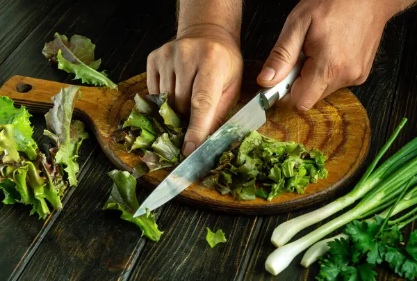 Taze sebzelerden salata hazırlıyorum. Mutfak tahtasına saplanmış bir bıçakla marul doğramak..