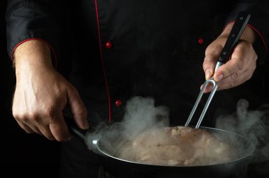 Şef sosisi tavada kızartırken elinde çatalla çeviriyor. Otel mutfağında sosis pişirme kavramı.