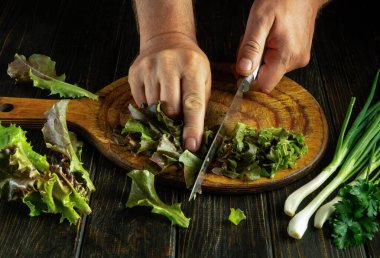 Elleri kesme tahtasının üzerinde vejetaryen yemeği hazırlayan bir aşçı. Marul yaprakları kesiyorum..