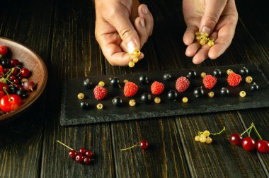 Olgun böğürtlenlerden lezzetli bir tatlı yapıyorum. Aşçı elleri siyah sıralama tahtasına üzümlü üzümler ekliyor..