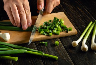 Bir adam, vejetaryen yemeklerine katmak için genç sarımsak saplarını bıçakla kesiyor..