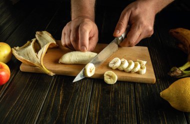 Mutfak tahtasındaki bıçakla olgun bir muzu doğramak. Kahvaltıda meyveli bir şefin elleriyle sağlıklı bir tatlı pişirmek. Muz diyeti.