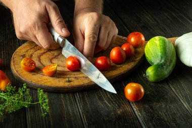 Şefin elleriyle sebze yemeği pişirmek için vişneli domates dilimliyorum. Mutfak masasında domatesli sebze diyeti konsepti.
