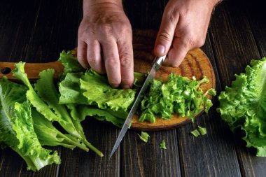 Vejetaryen menüsü hazırlamak için marul kesiyorum. Mutfak tahtasındaki marul yapraklarını kestiği için bir şefin elinde bıçak..
