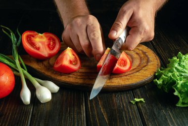 Mutfak masasında taze domates hazırlıyorum. Aşçı, sebze salatası hazırlamak için domatesi tahta bir bıçakla kesiyor..