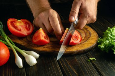 Bir aşçının elleriyle domatesli ve soğanlı bir yemek pişirmek. Domates doğradığı için şefin elinde bir bıçak..