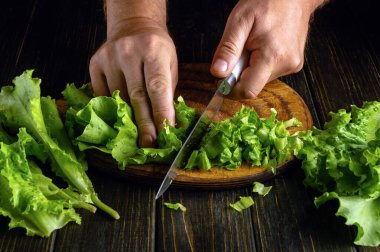 Salata yapmadan önce marul yaprakları kesiyorum. Bıçak bizzat mutfak masasının üzerinde..