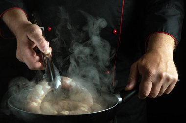 Kızartma tavasında et sosisi pişiren şefin yakın çekimi. Mutfakta et yemeği pişirmek gibi basit bir kavram..